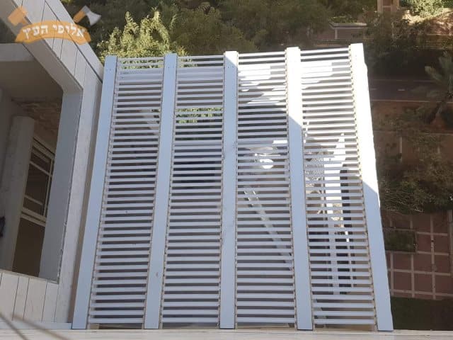 פרגולה לבנה מעץ מותקנת במרפסת שמש בדירה בקרית מוצקין כולל הצללה מלייסטים. צילום: שחר